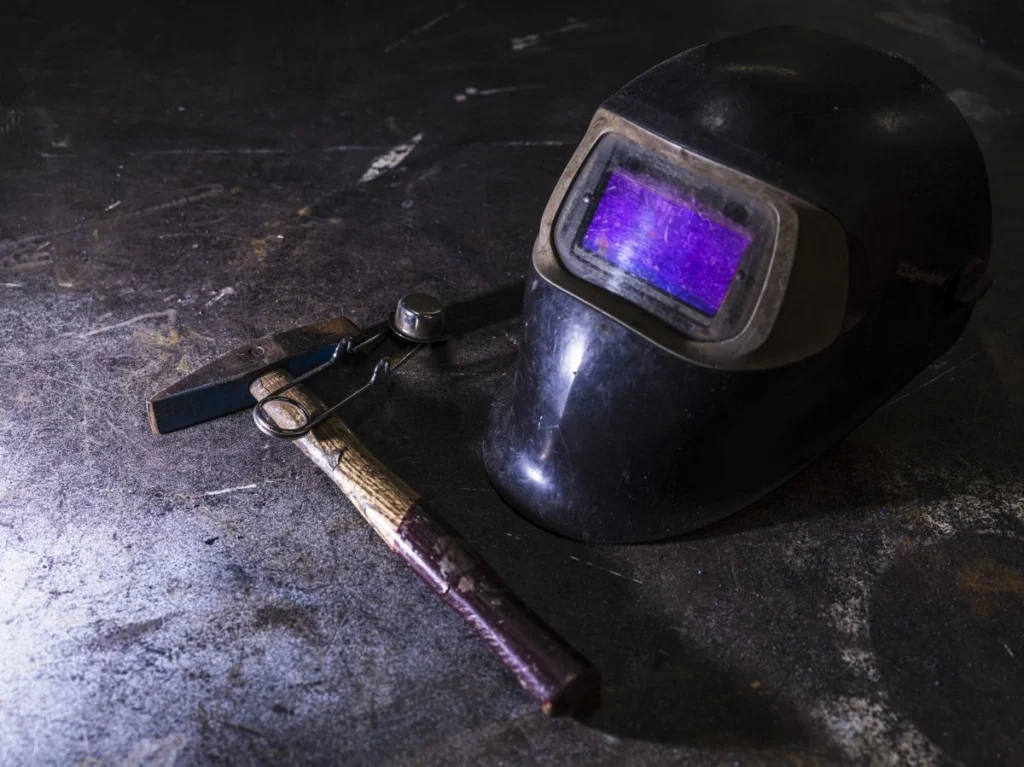 Gros plan d’un masque de soudure automatique LCD posé à côté d’un marteau sur un établi métallique
