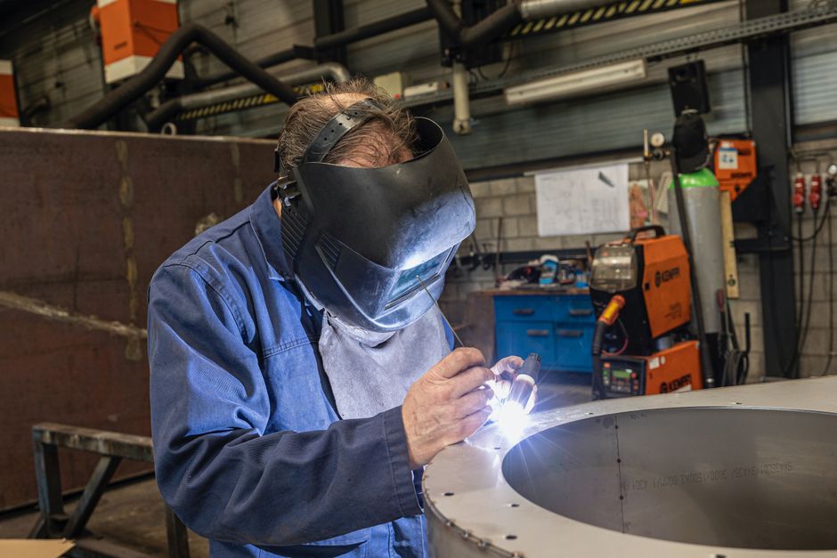 Soudeur TIG travaillant sur une virole inox, bouteille d’argon et poste en arrière-plan