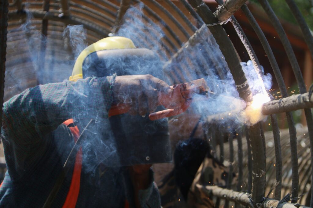 Soudeur à l’électrode avec masque, fumée et étincelles sur une structure en acier